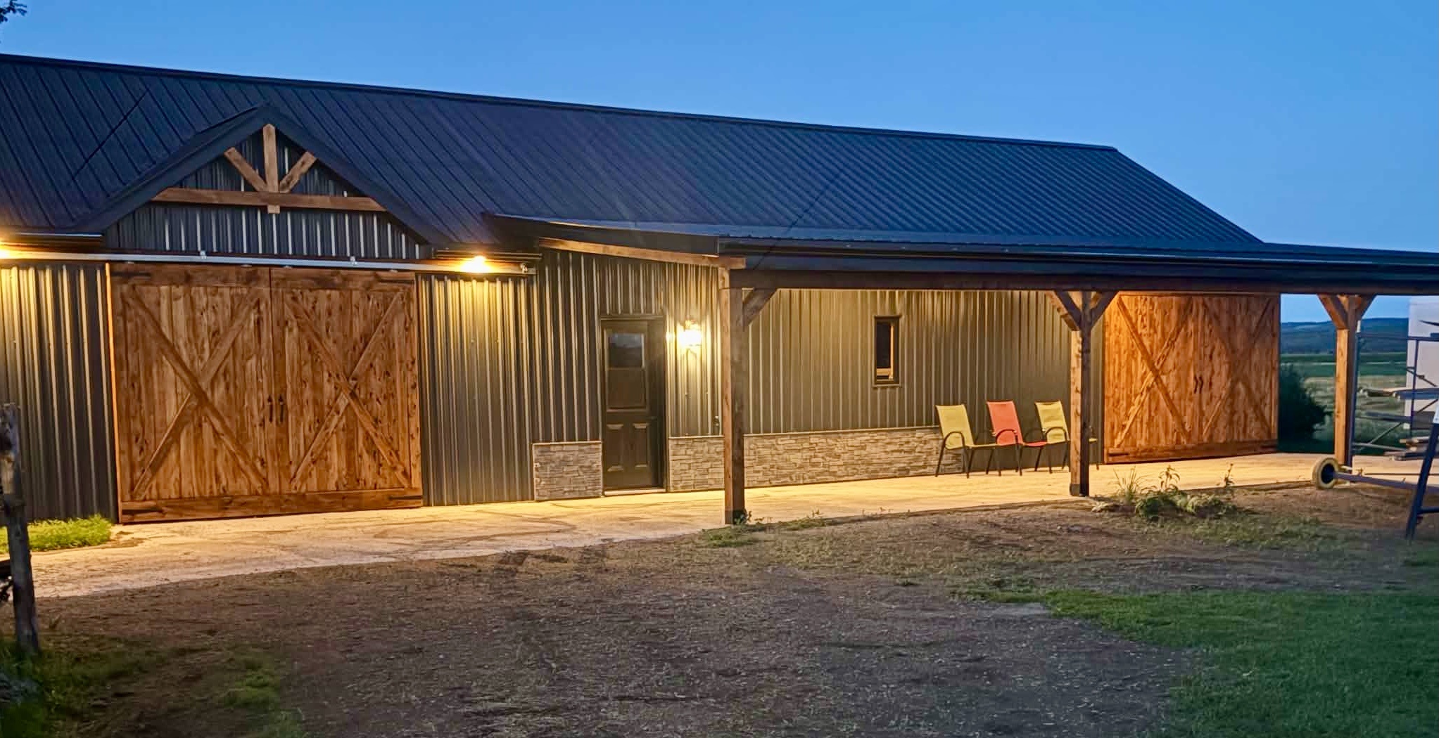 Construction neuve d’un garage avec toit et murs de tôle gris métalliques foncés avec 2 larges portes de bois et 3 colonnes de soutien. La terrasse est sur plancher de ciment coulé.